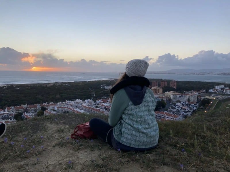 Frau sitzt vor Stadt und Sonnenuntergang